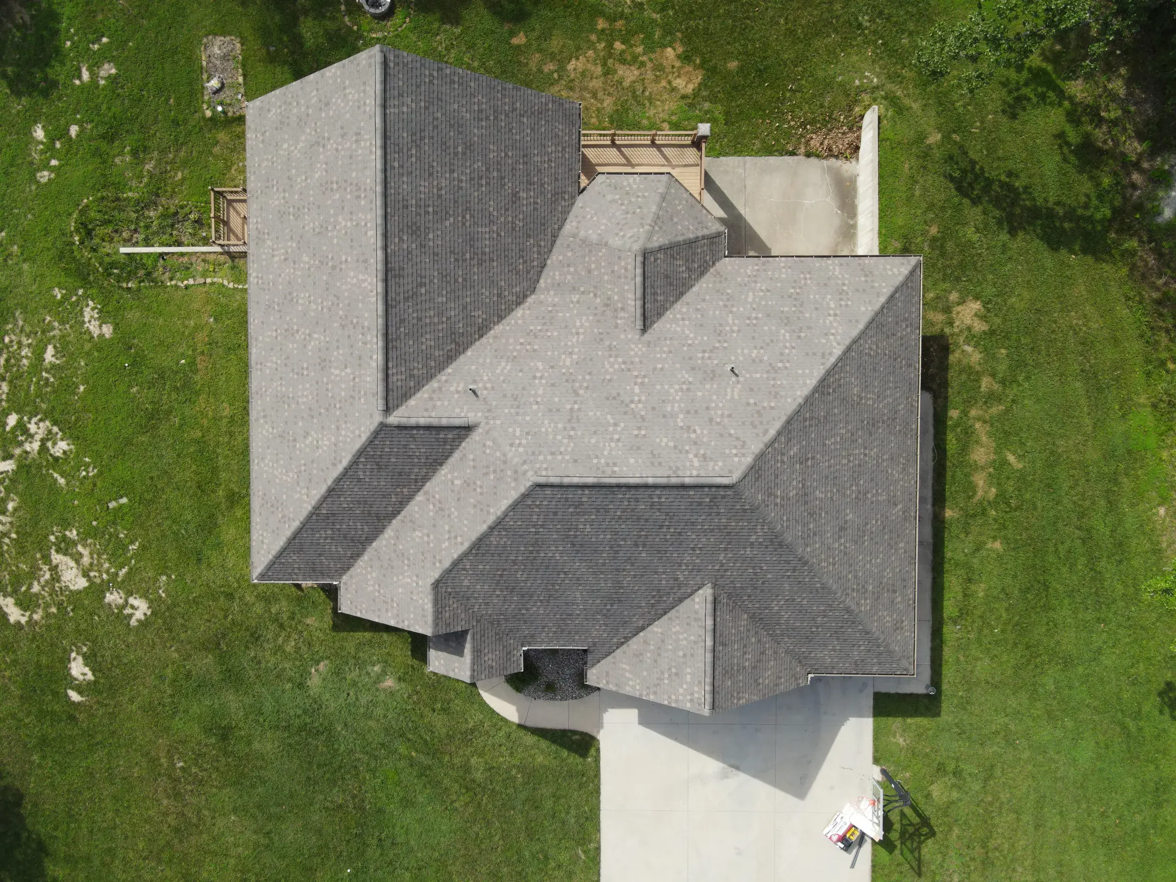 Overhead drone view of a finished gray asphalt shingle roof with multiple gables on a green lawn.