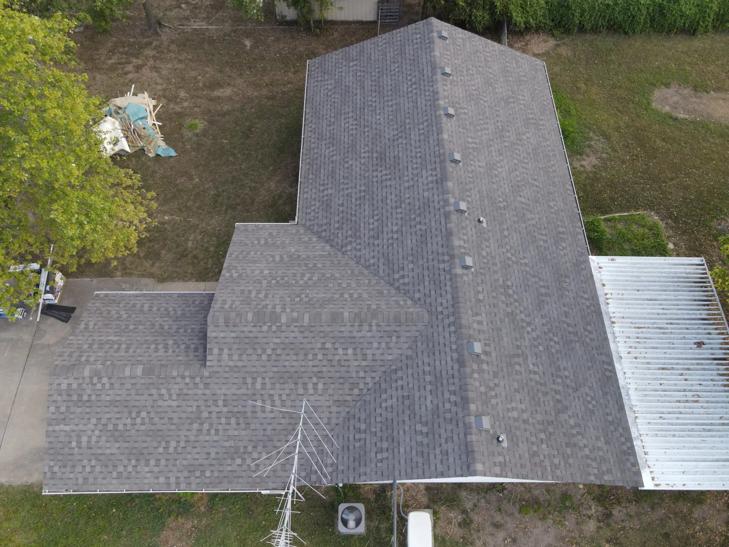 An overhead drone view of a long house with a newly installed gray asphalt shingle roof, box vents lined along one slope.