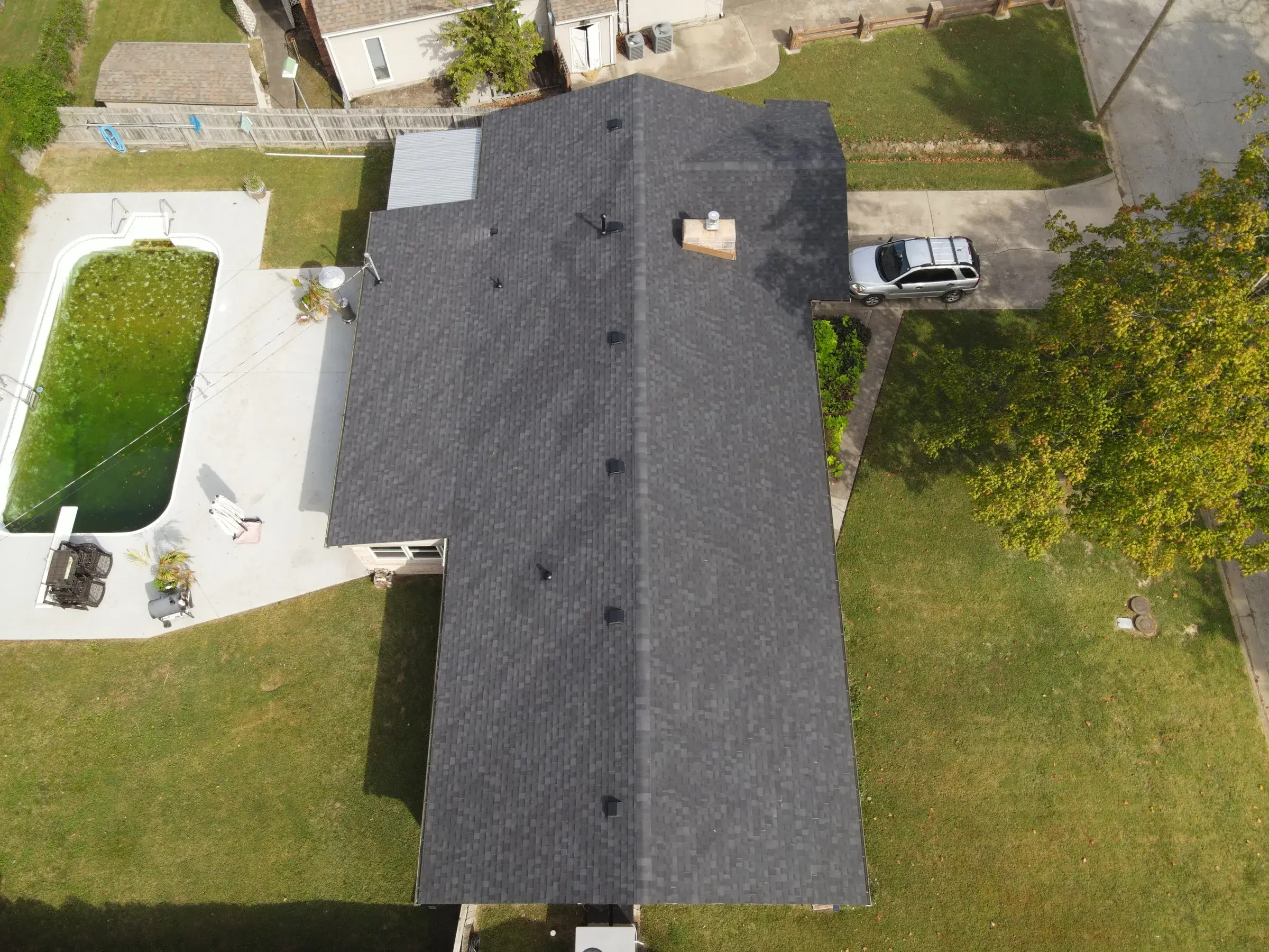 Aerial view of a house with a newly shingled dark gray roof, with a backyard pool and driveway visible below.