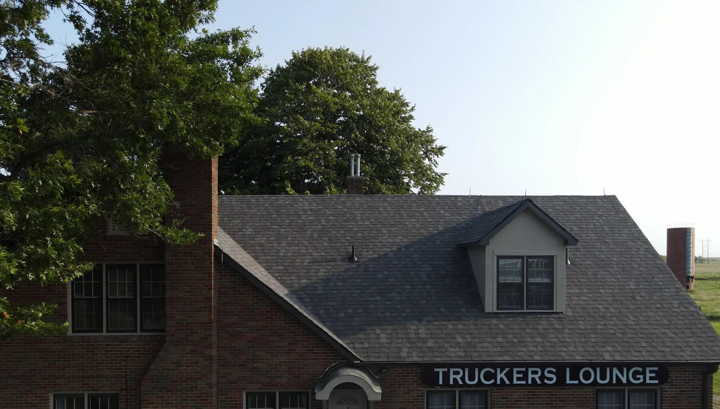 A completed charcoal architectural shingle roof with a dormer on a two-storey brick commercial building, seen from an elevated angle.